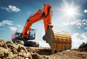 A large orange digger with its bucket resting on the ground, positioned on a construction site under a bright, sunny sky.