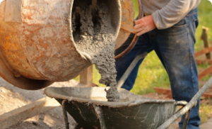 A construction worker is pouring wet concrete from a cement mixer into a wheelbarrow.