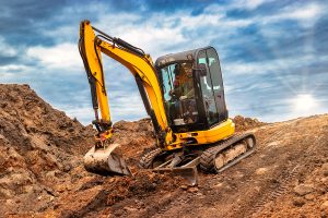 Mini excavator at the construction site on the edge of a pit against a cloudy blue sky. Compact construction equipment for earthworks. An indispensable assistant for earthworks